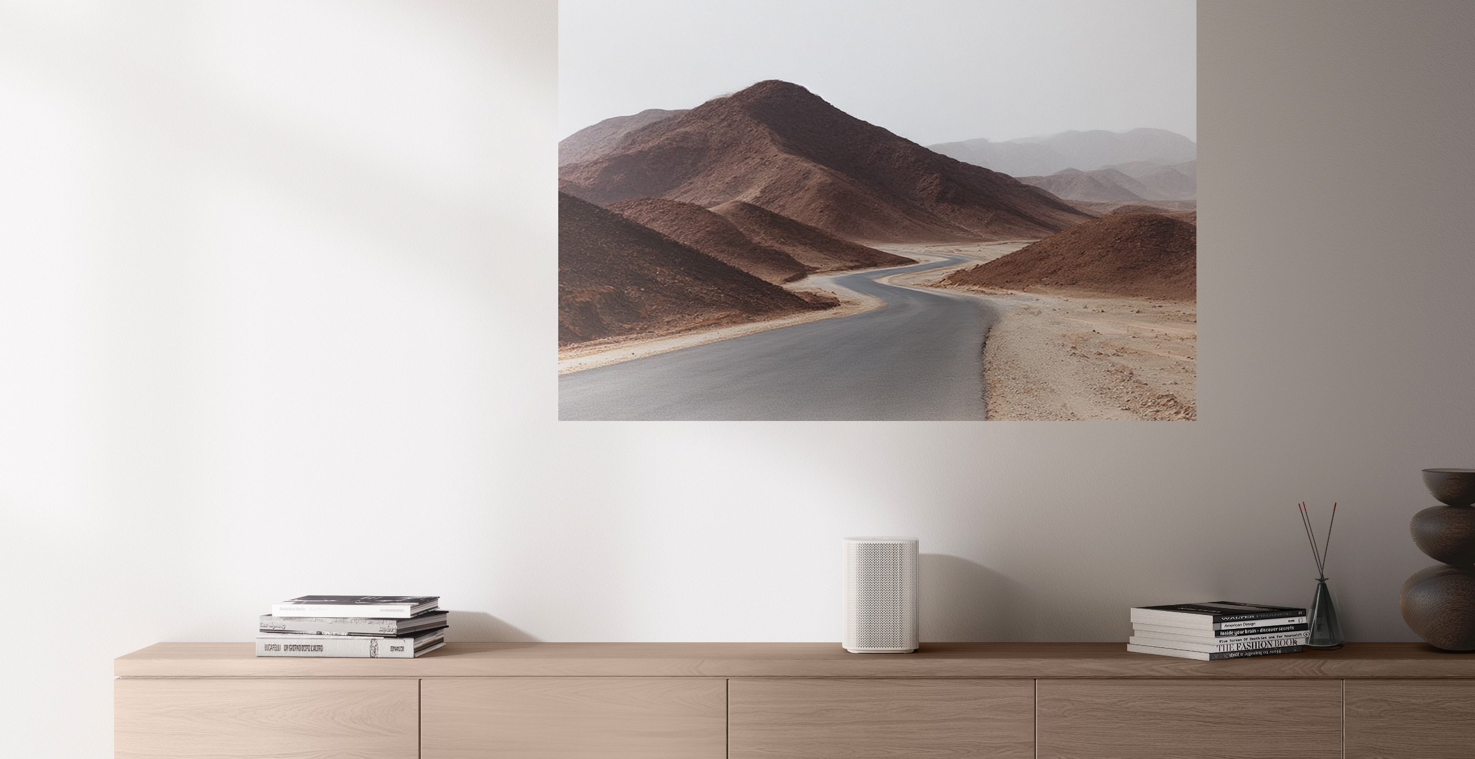 On a light wooden shelf, books and a small speaker are placed. A projected image on the wall shows a scenic mountain view. Sunlight softly illuminates the space.
